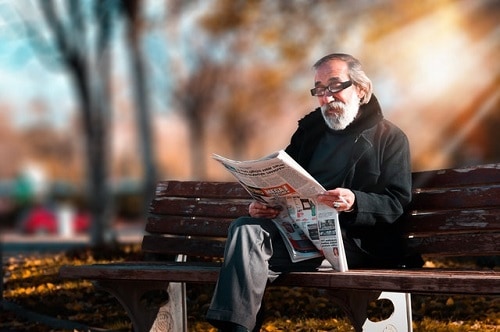 older man reading on park bench